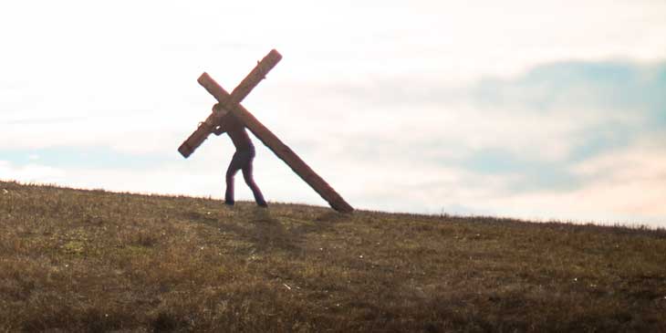 silhouette of person carrying a cross against a bright sky