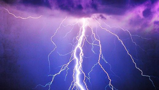 A brilliant flash of lightning illuminates a dark violet blue sky