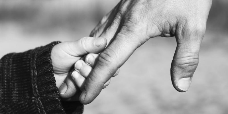 a small child's hand holds to the finger of a man